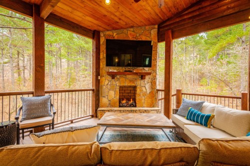 Cozy outdoor seating area with a stone fireplace and TV, surrounded by trees in a serene setting.