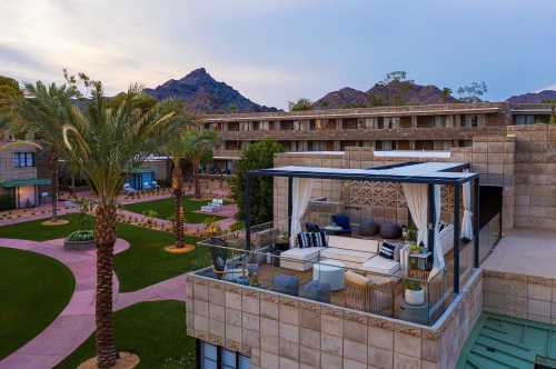 A luxurious outdoor lounge area with seating, surrounded by palm trees and mountains, at a modern resort.