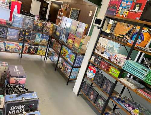 A game store interior featuring shelves filled with various board games and tabletop games.