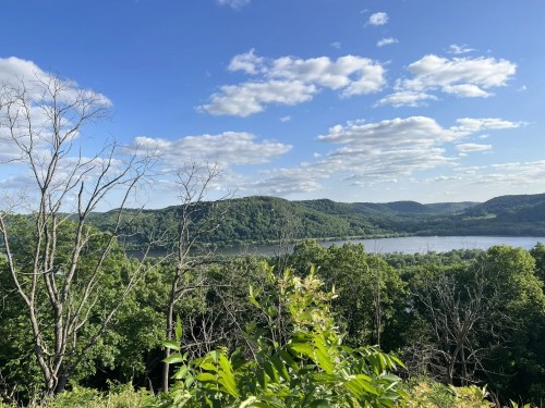 A scenic view of a river surrounded by lush green hills under a partly cloudy sky.