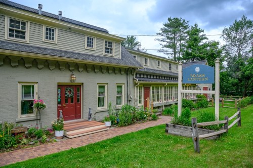 A charming building with a sign reading "Brass Lantern," surrounded by greenery and a pathway.