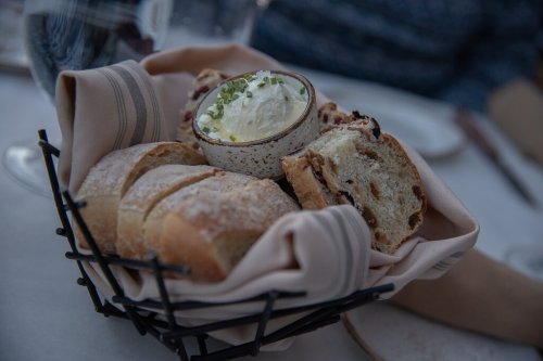 A basket of assorted bread rolls with a small bowl of creamy dip, garnished with chives, on a dining table.