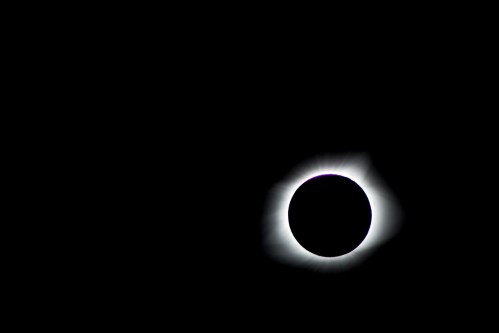 A solar eclipse with a darkened sun surrounded by a glowing halo against a black sky.