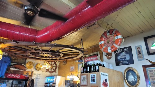 Interior of a nautical-themed restaurant featuring a ship's wheel, red ductwork, and vintage decor.