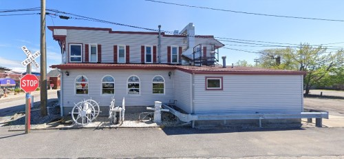 A two-story building with a red roof, large windows, and a stop sign in front, set in a rural area.