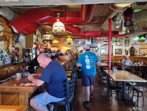 A cozy restaurant interior with a bar, patrons seated at tables, and colorful decor, creating a warm atmosphere.