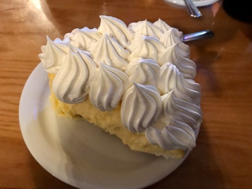 A slice of creamy lemon pie topped with fluffy whipped cream, served on a white plate.