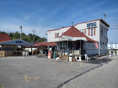 A two-story building with a red roof, featuring a sign that reads "Bar Harbor" and outdoor seating in a parking lot.