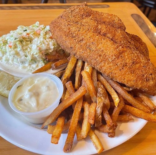 A plate featuring crispy fried fish, coleslaw, and a side of golden French fries with a dipping sauce.