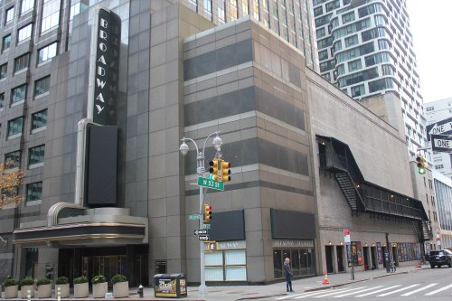 Broadway theater exterior with a marquee, modern buildings, and a street corner in an urban setting.
