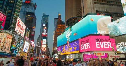 Crowd in Times Square, New York, surrounded by bright billboards and skyscrapers at dusk.