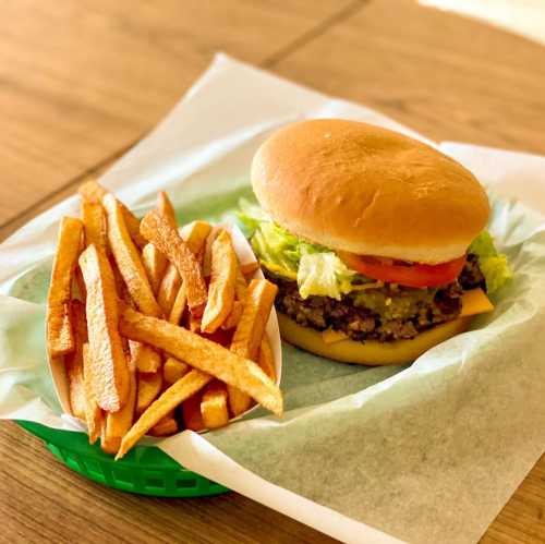 A delicious burger with lettuce and tomato, served with a side of crispy French fries on a green tray.