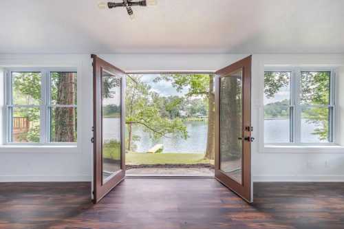 A view of a serene lake through open double doors, framed by large windows and surrounded by greenery.