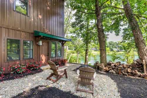 Cozy outdoor seating area with two chairs by a lake, surrounded by trees and colorful flowers.