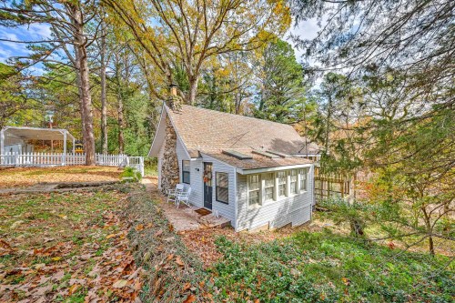 A charming cottage surrounded by autumn foliage and trees, featuring a stone exterior and a cozy porch.
