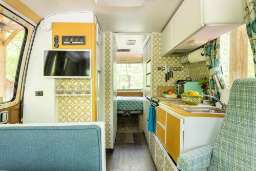 Interior of a cozy camper van featuring a kitchenette, seating area, and a view of a bedroom in the background.
