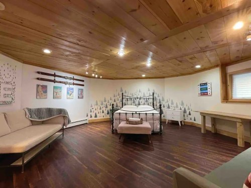 Cozy room with wooden ceiling, a bed, a sofa, and decorative wall art featuring trees and colorful designs.