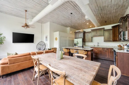 Modern kitchen and dining area with wooden table, brown sofa, and large windows, featuring a cozy, open layout.