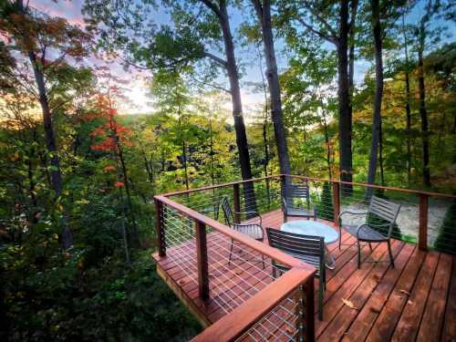 A wooden deck surrounded by trees, featuring a table and chairs, with a colorful sunset in the background.