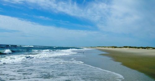 A serene beach scene with gentle waves, soft sand, and a clear blue sky.