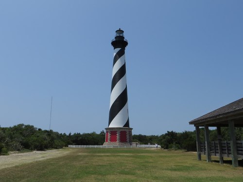 A tall black and white striped lighthouse stands in a grassy area under a clear blue sky.