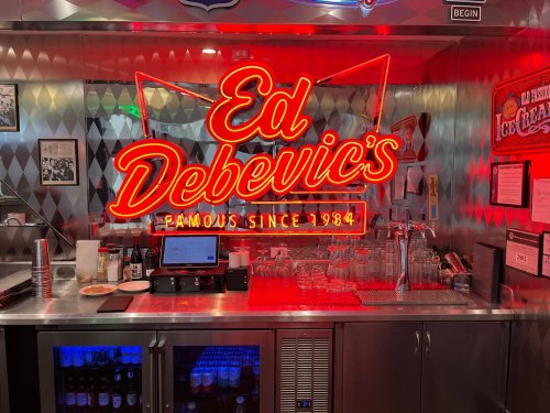 Neon sign for Ed Debevic's, a diner, with a metallic backdrop and illuminated bar area.