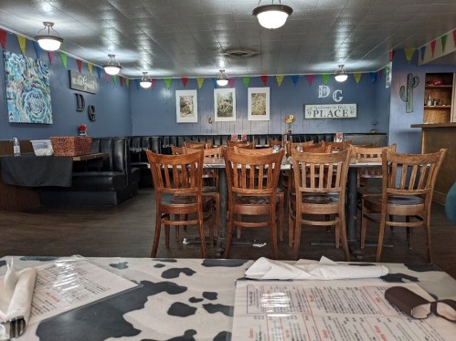 Interior of a restaurant featuring wooden chairs, colorful bunting, and a cozy dining area with tables set for guests.