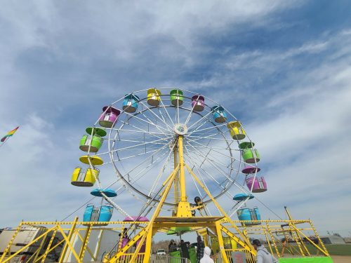 A colorful Ferris wheel with yellow and pastel-colored gondolas against a blue sky with scattered clouds.