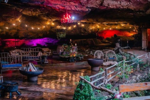 A cozy cave interior with colorful lights, seating areas, and decorative plants, creating a warm, inviting atmosphere.