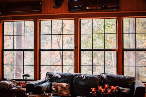 Cozy interior with a black couch and large windows showcasing a forest view in autumn.