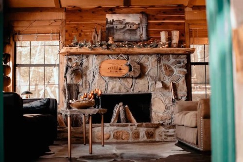 Cozy cabin interior featuring a stone fireplace, wooden decor, and comfortable seating. Warm, inviting atmosphere.