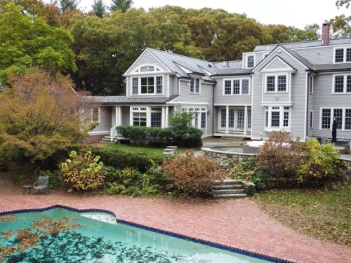 A spacious gray house with large windows, surrounded by trees and a pool with fallen leaves in the backyard.