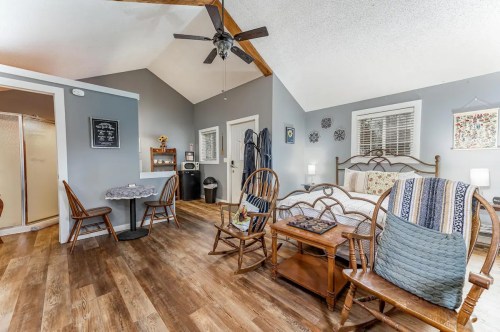 Cozy room with a bed, seating area, and dining table, featuring wooden accents and a ceiling fan.