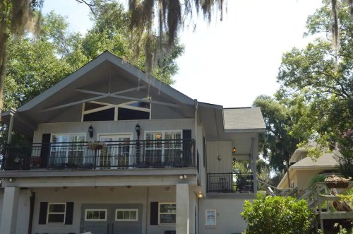 A two-story house with a balcony, surrounded by trees and hanging moss, under a clear blue sky.