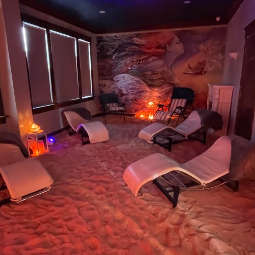 A serene spa room with lounge chairs, soft lighting, and a calming mural on the wall, creating a relaxing atmosphere.