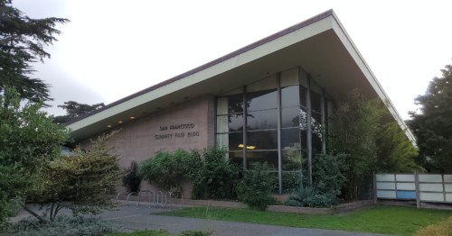 Exterior view of the San Francisco Community Fair Building, featuring large windows and surrounding greenery.
