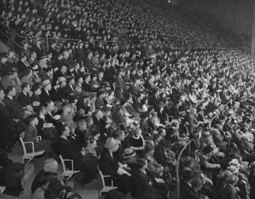 A large crowd of people seated in a stadium, many wearing hats, attentively watching an event.