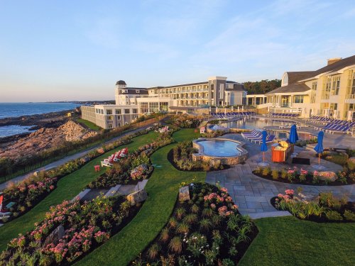 A coastal resort with landscaped gardens, a pool, and lounge chairs overlooking the ocean at sunset.