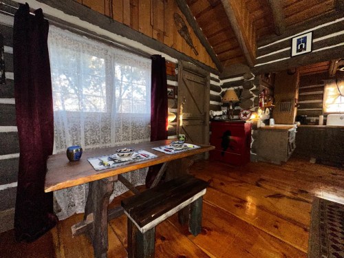 Cozy log cabin interior featuring a wooden table, bench, and rustic decor with a window letting in natural light.