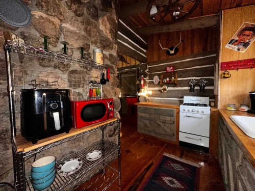 Cozy kitchen with stone walls, wooden accents, and appliances like a microwave and stove, featuring rustic decor.