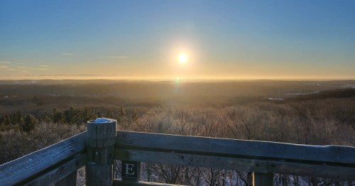 A scenic view from a wooden lookout, featuring a sunrise over a misty landscape and distant mountains.