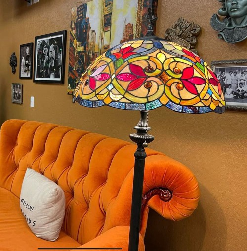 A colorful stained glass lamp stands beside an orange couch in a cozy, decorated living space.