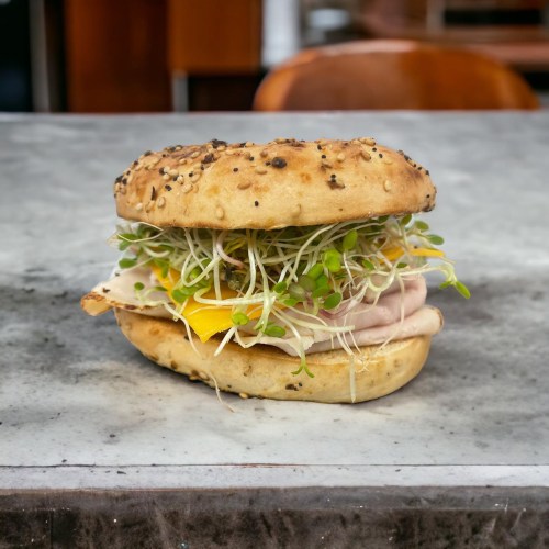 A sesame seed bagel filled with turkey, sprouts, and a slice of cheese, resting on a marble surface.