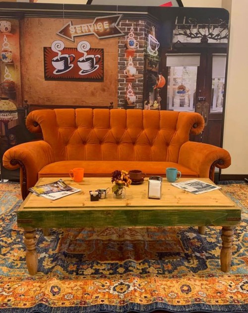 A cozy orange sofa with a wooden coffee table, surrounded by decorative items and a colorful rug in a warm setting.