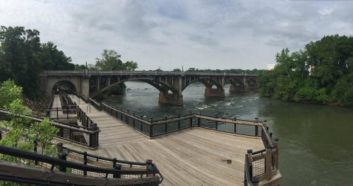 A panoramic view of a bridge over a river, with wooden walkways and lush greenery along the banks.