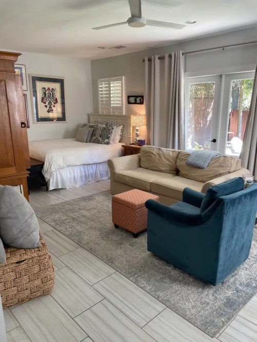 Cozy living space featuring a sofa, armchair, bed, and natural light from large windows.