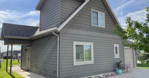 A modern gray house with a peaked roof, featuring a small porch and a garage, set against a clear blue sky.