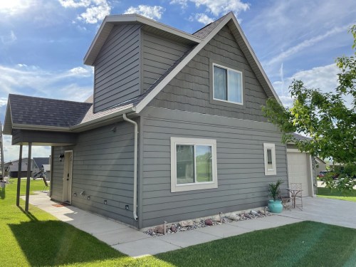 A modern gray house with a sloped roof, large windows, and a well-maintained lawn under a blue sky.