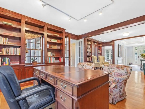 A cozy home office with wooden bookshelves, a desk, and floral-patterned sofas, featuring bright lighting and a welcoming atmosphere.