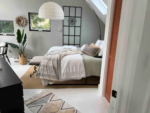 Cozy bedroom with a bed, decorative pillows, a woven rug, and natural light from a skylight.
